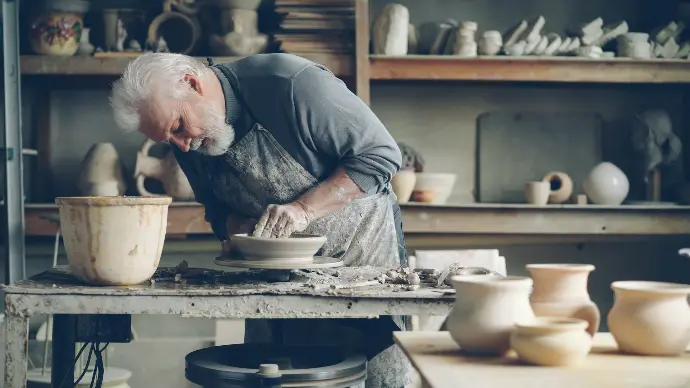An elderly potter shapes clay on a wheel.